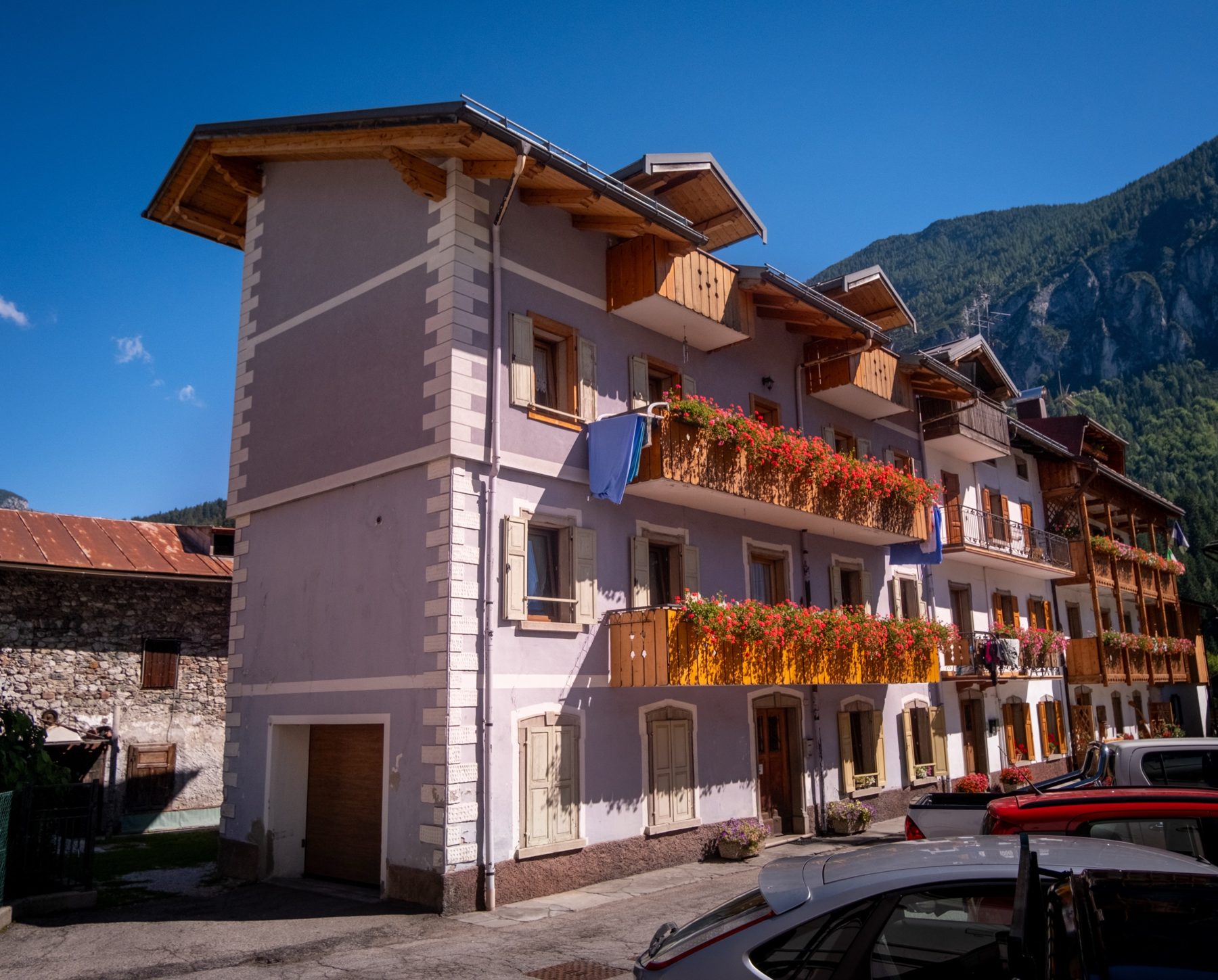 Casa Bagatin vista dall'esterno, con i balconi in legno fioriti e le montagne alle spalle